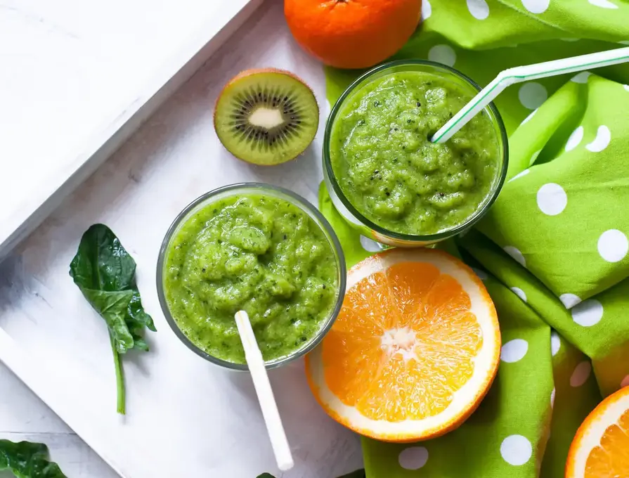 fresh green smoothie on tray with kiwi and orange slice